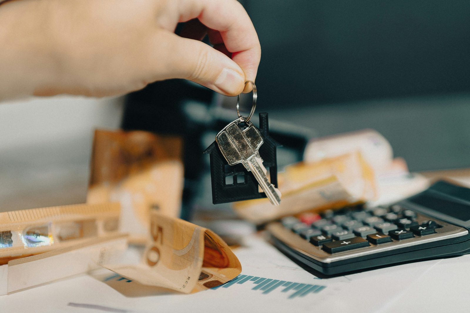 Hand holding a house key beside a calculator for how much property management charges